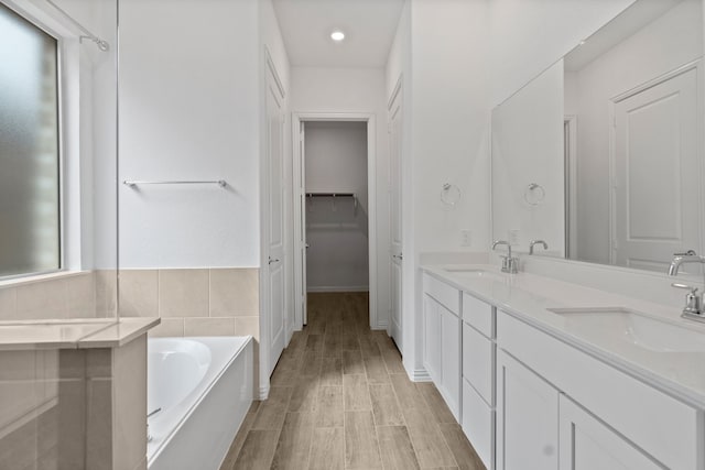 bathroom with double vanity, a bath, tile walls, and a walk in closet