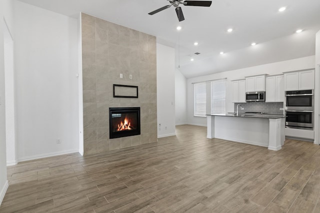 unfurnished living room featuring ceiling fan, baseboards, light wood finished floors, a fireplace, and vaulted ceiling