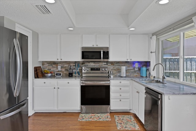 kitchen featuring appliances with stainless steel finishes, a sink, light wood finished floors, white cabinets, and recessed lighting