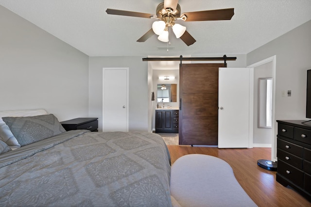 bedroom with a barn door, wood finished floors, ensuite bathroom, and a ceiling fan