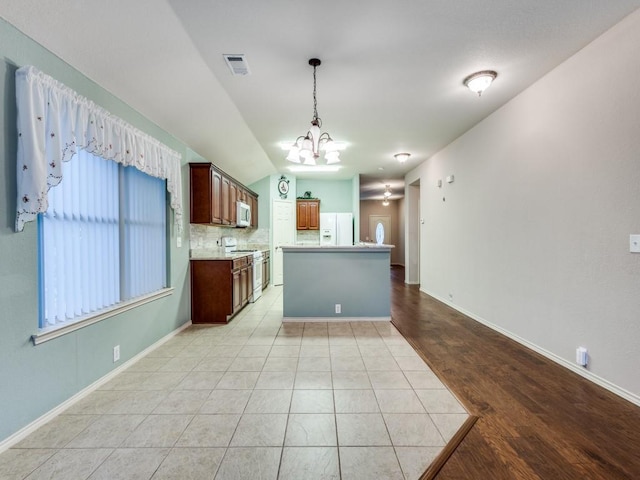 kitchen featuring white appliances, a chandelier, tasteful backsplash, light countertops, and hanging light fixtures