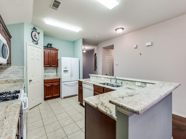 kitchen with a sink, white appliances, a large island with sink, decorative backsplash, and light stone counters