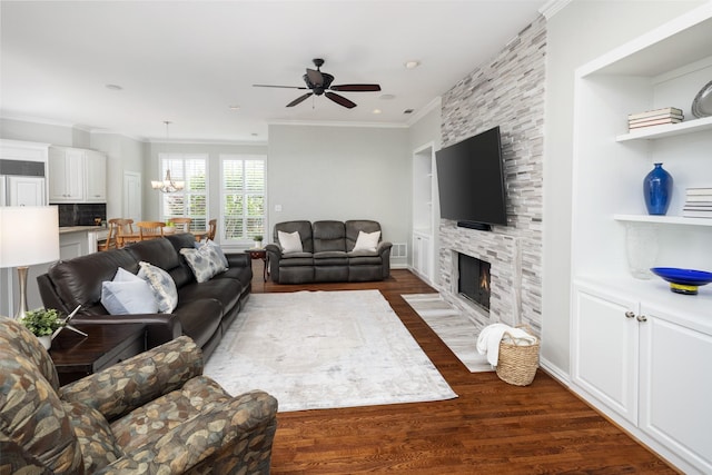 living area with crown molding, a chandelier, ceiling fan, a fireplace, and dark wood-style flooring