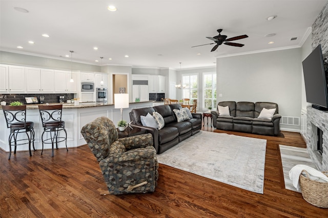 living area with crown molding, a fireplace, a ceiling fan, a chandelier, and dark wood-type flooring