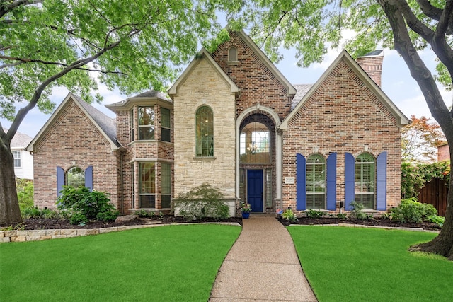 view of front of property featuring a front yard, brick siding, a chimney, and stone siding
