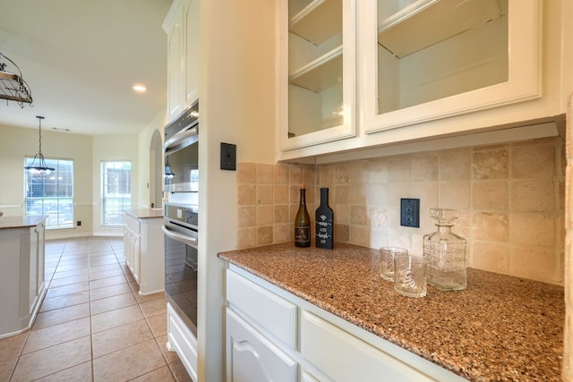 kitchen featuring stainless steel oven, backsplash, light tile patterned floors, glass insert cabinets, and white cabinetry