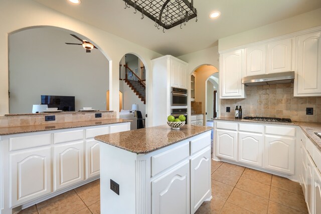 kitchen featuring arched walkways, under cabinet range hood, stainless steel appliances, a center island, and light tile patterned floors
