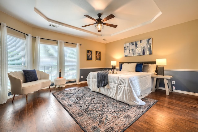 bedroom featuring a tray ceiling, wood finished floors, baseboards, and ceiling fan