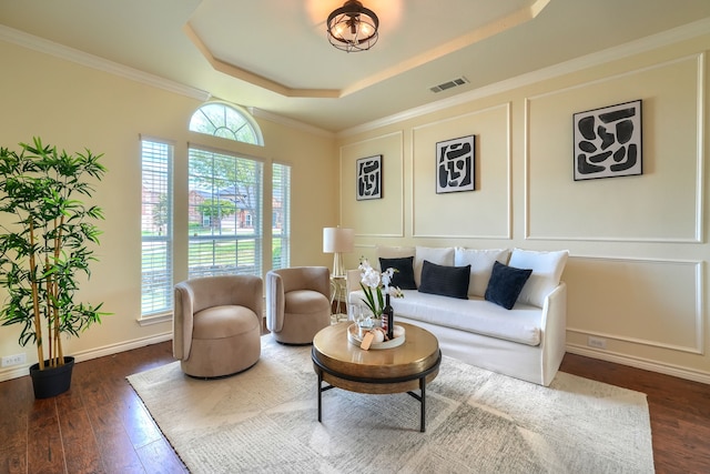 living area featuring a raised ceiling, dark wood-style flooring, a decorative wall, baseboards, and crown molding
