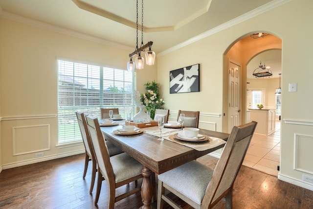 dining room with arched walkways, dark wood-style floors, a tray ceiling, ornamental molding, and a chandelier