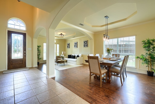 tiled dining room with a raised ceiling, a chandelier, ornamental molding, arched walkways, and baseboards