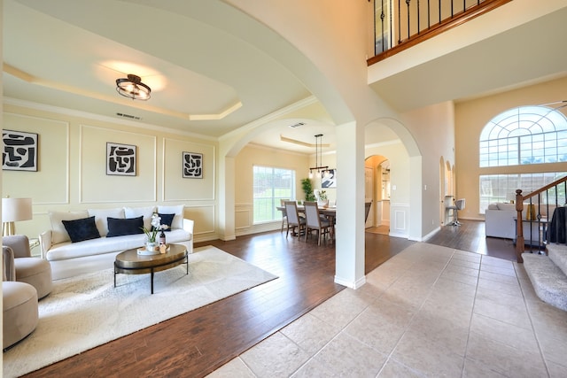 living room featuring a decorative wall, arched walkways, a tray ceiling, ornamental molding, and a towering ceiling