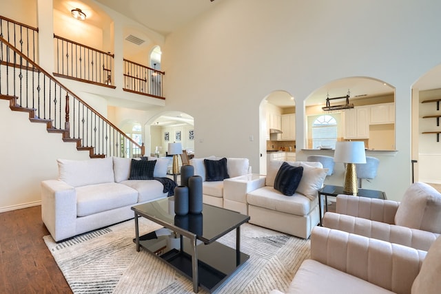 living area with wood finished floors, arched walkways, a towering ceiling, stairs, and baseboards