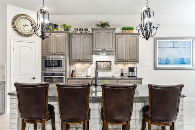 121 Quail Run Rd, Red Oak, TX 75154 - kitchen featuring stainless steel appliances, a chandelier, decorative backsplash, light stone counters, and a center island with sink