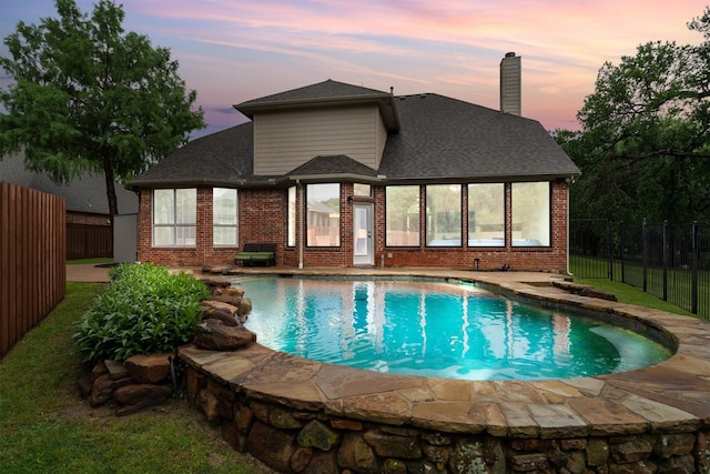 pool at dusk with a fenced backyard