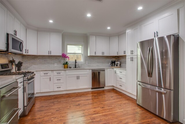 4719 Wateka Dr, Dallas, TX 75209 - kitchen featuring appliances with stainless steel finishes, a sink, white cabinets, decorative backsplash, and light wood-style flooring