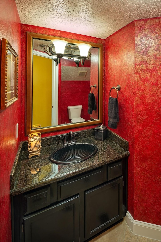 half bathroom featuring a textured ceiling, vanity, and toilet
