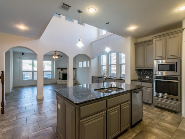 928 Freesia Dr, Little Elm, TX 75068 - kitchen with appliances with stainless steel finishes, a sink, arched walkways, a fireplace with raised hearth, and a kitchen island with sink