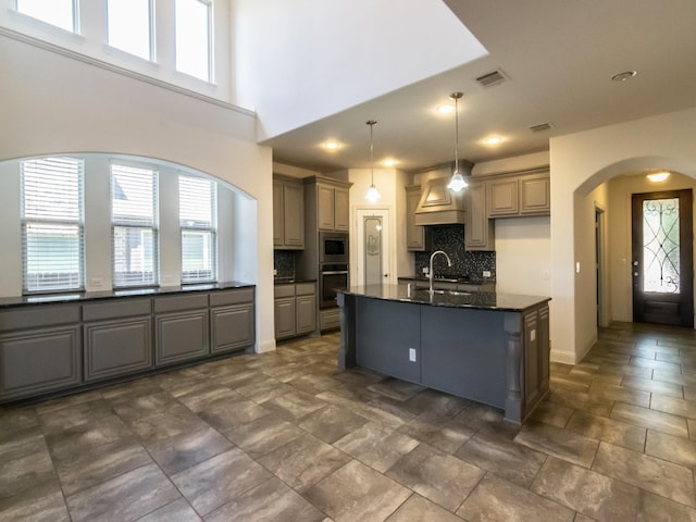928 Freesia Dr, Little Elm, TX 75068 - kitchen featuring stainless steel appliances, arched walkways, decorative backsplash, a center island with sink, and gray cabinets