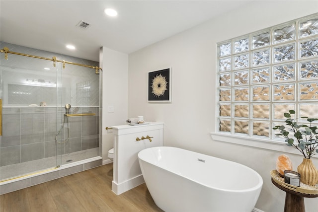 bathroom featuring a stall shower, wood finished floors, a freestanding bath, toilet, and recessed lighting