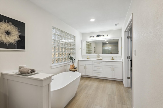 bathroom with wood finished floors, a soaking tub, double vanity, and recessed lighting