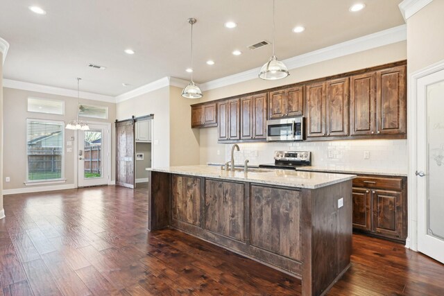 kitchen with stainless steel appliances, a sink, decorative backsplash, a barn door, and an island with sink