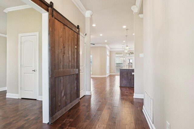 hallway with a barn door, crown molding, dark wood finished floors, baseboards, and recessed lighting