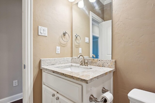 half bathroom with vanity, toilet, and a textured wall