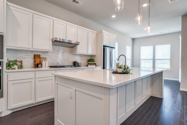 3001 Renmuir Dr, Prosper, TX 75078 - kitchen featuring appliances with stainless steel finishes, under cabinet range hood, backsplash, white cabinetry, and an island with sink
