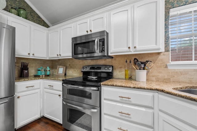 kitchen featuring stainless steel appliances, ornamental molding, white cabinets, light stone counters, and vaulted ceiling