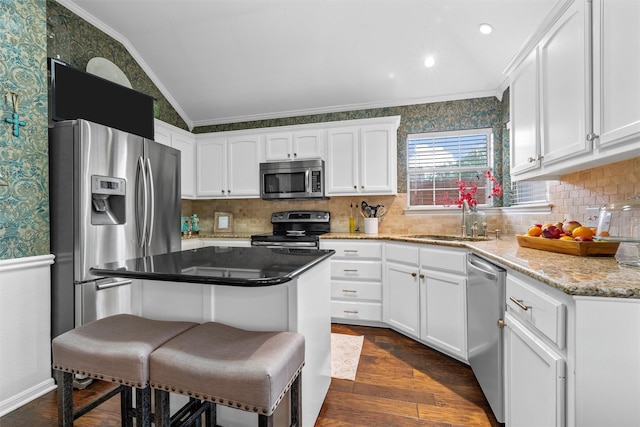 kitchen with stainless steel appliances, a sink, crown molding, vaulted ceiling, and white cabinetry