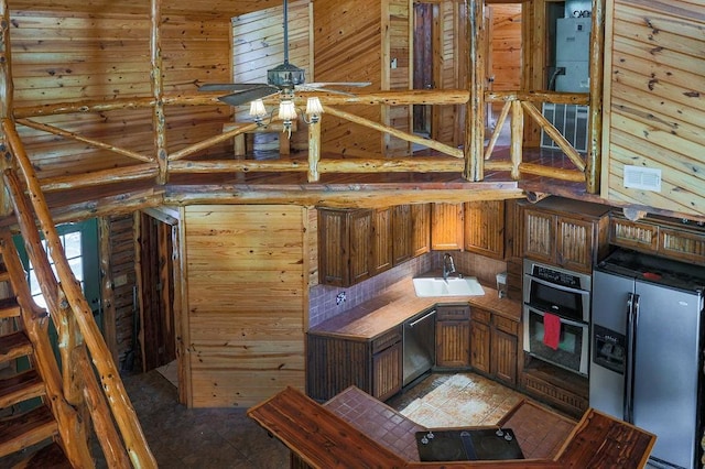 kitchen with stainless steel appliances, a sink, a ceiling fan, wooden walls, and light tile patterned floors