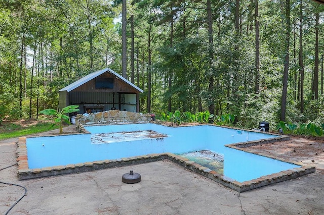view of swimming pool with a swimming pool, a patio, an outdoor structure, and a wooded view