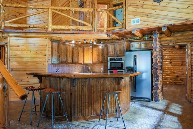 kitchen with appliances with stainless steel finishes, a high ceiling, a sink, log walls, and a kitchen breakfast bar