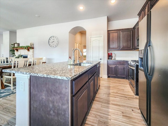 1152 Snowy Owl Dr, Alvarado, TX 76009 - kitchen featuring stainless steel appliances, a sink, light wood-style flooring, dark brown cabinets, and a center island with sink