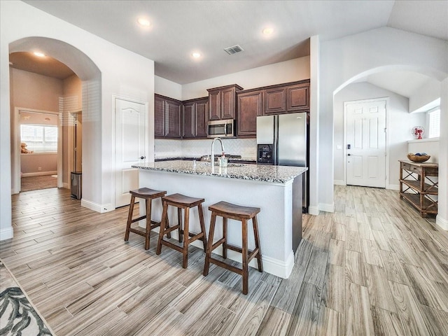 1152 Snowy Owl Dr, Alvarado, TX 76009 - kitchen with stainless steel microwave, light wood finished floors, fridge with ice dispenser, dark brown cabinets, and arched walkways