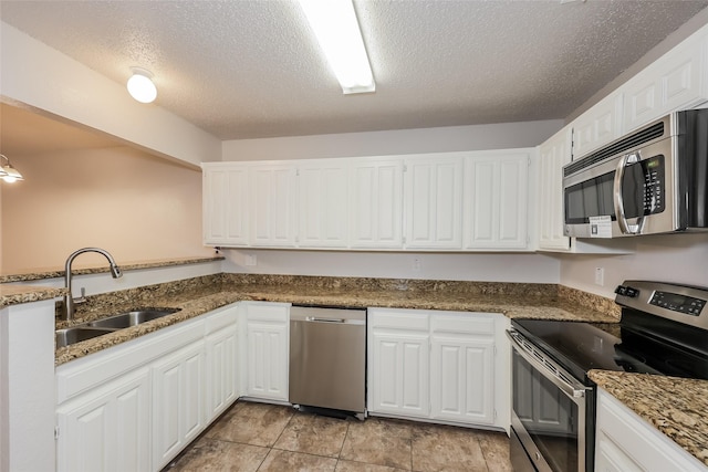 kitchen featuring appliances with stainless steel finishes, a sink, a textured ceiling, white cabinetry, and dark stone counters