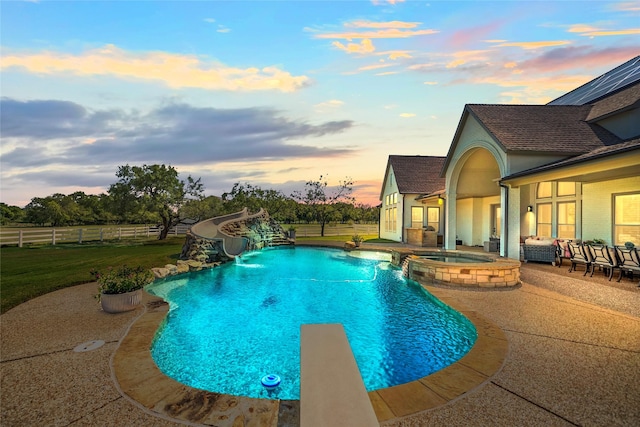 view of pool with a water slide, a patio, fence, a diving board, and a pool with connected hot tub