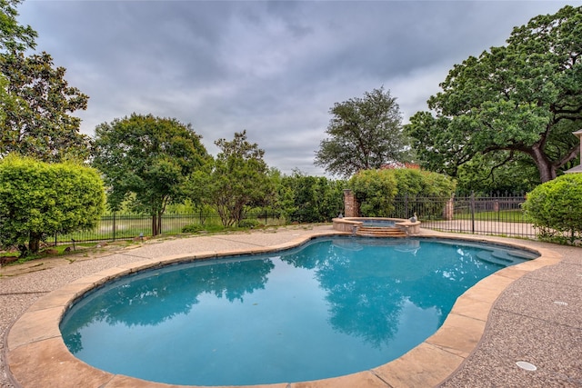 view of pool with fence, a pool with connected hot tub, and view of wooded area
