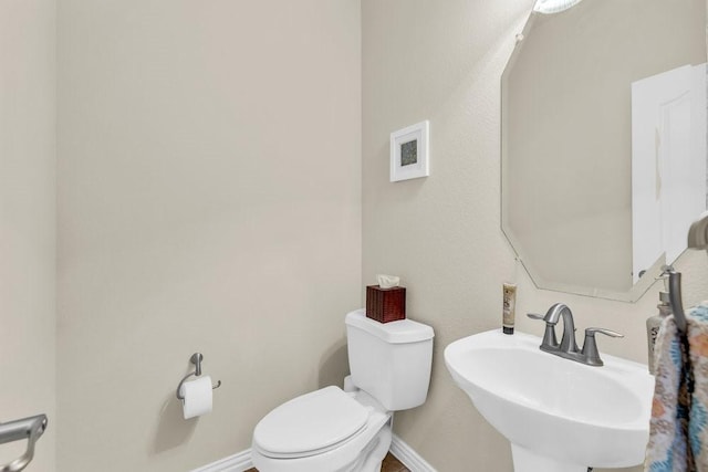 half bathroom featuring a sink, toilet, and baseboards