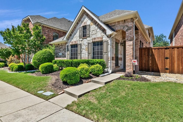 french country style house with stone siding, a shingled roof, and brick siding