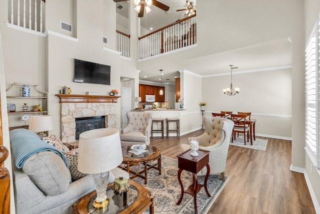 living room with ceiling fan, baseboards, plenty of natural light, a stone fireplace, and ornamental molding