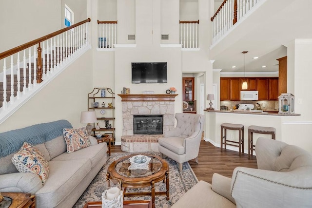 living area featuring a towering ceiling, wood finished floors, stairway, a stone fireplace, and recessed lighting