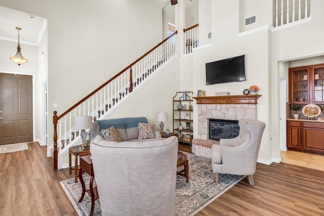 living room with a towering ceiling, stairway, wood finished floors, a stone fireplace, and baseboards