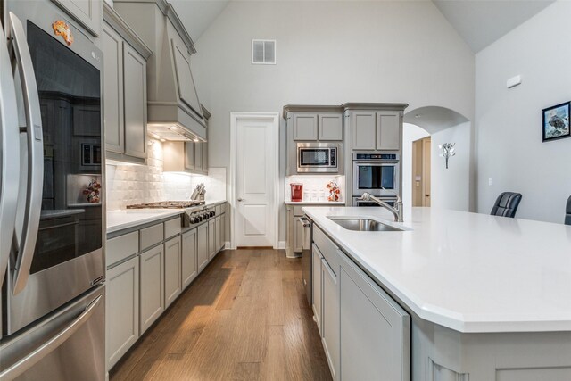kitchen with a sink, gray cabinetry, stainless steel appliances, high vaulted ceiling, and wood finished floors