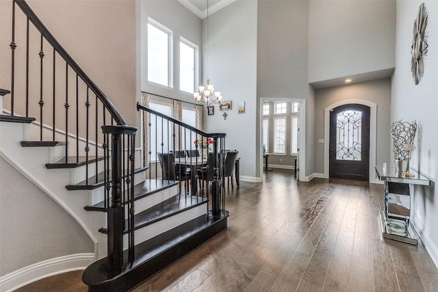 entryway with stairs, a chandelier, a towering ceiling, baseboards, and wood finished floors