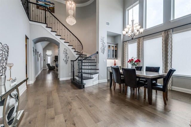 dining room with stairway, a chandelier, wood finished floors, arched walkways, and a high ceiling