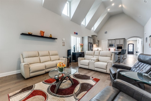 living area featuring high vaulted ceiling, arched walkways, light wood-type flooring, and baseboards