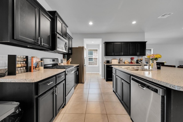 kitchen featuring appliances with stainless steel finishes, a sink, dark cabinetry, light tile patterned flooring, and recessed lighting