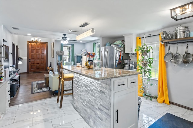 741 N Robinson St, Cleburne, TX 76031 - kitchen featuring freestanding refrigerator, light marble finish flooring, white cabinets, and a breakfast bar